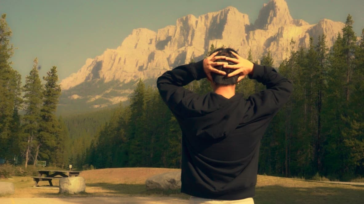 Jason with his hands on his head, facing sunlit mountains