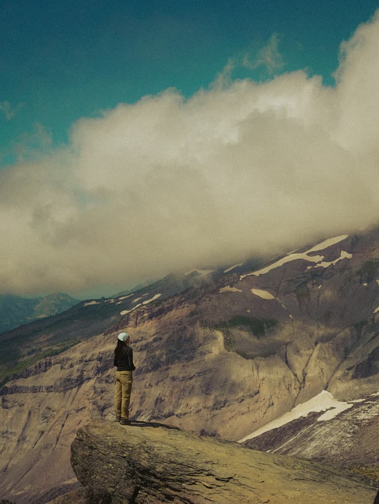 A lone hiker on a snowy ridge under rolling clouds